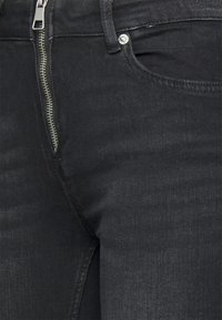 Jeans de ganga preta com fecho de correr, design de cinco bolsos e uma textura subtil, apresentando um corte justo.