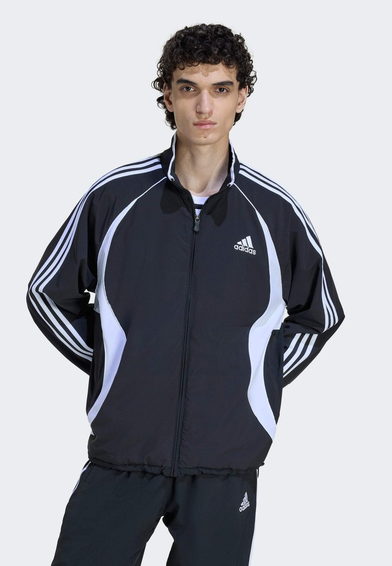 Melns zipa jaka ar baltām akcentiem un trim svītrām uz piedurknēm. Izgatavota no gludas auduma, ar augstu apkakli un kabatām.