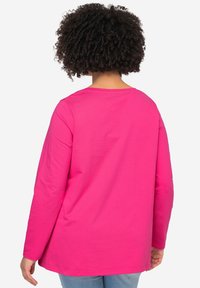 Camisa de manga larga en algodón de un vibrante color rosa, con un cuello redondo sencillo y un corte relajado, con un bajo recto en la cintura y sin adornos adicionales.