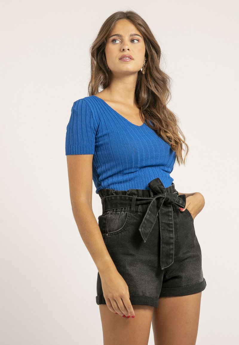 Haut en tricot côtelé bleu avec des manches courtes et un col en V, associé à des shorts en denim noir taille haute dotés d'une ceinture nouée et d'ourlets retournés.