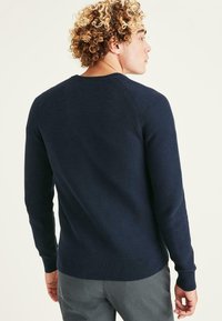 Pull en marine à mailles texturées, avec un col rond et des poignets et un ourlet côtelés. Présenté de dos, avec une coupe relaxée.