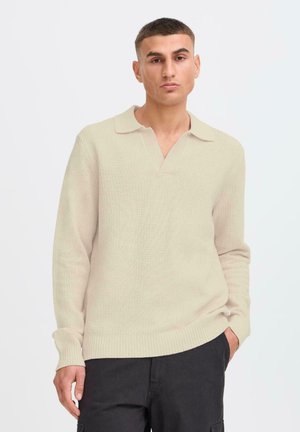 Beige textured knit pullover with a V-neck and collar, featuring long sleeves and ribbed cuffs. Worn with dark trousers.
