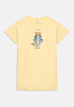 Tricou galben cu mâneci scurte, cu un urs care poartă o pălărie, o jachetă din denim, pantaloni cu dungi și ține un coș cu flori în față.