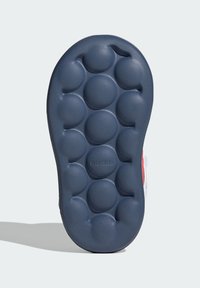 Suola di una scarpa realizzata in materiale gommoso di colore blu scuro, con strutture arrotondate simili a bolle e il logo adidas impresso vicino al tallone.