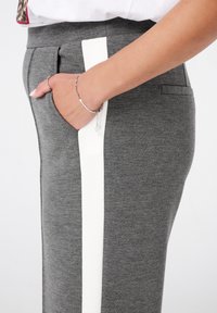 Grijze gebreide broeken met een witte verticale streep, voorzien van zijzakken en een getailleerde pasvorm. Het materiaal lijkt zacht met een lichte textuur.