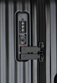 Valigia rigida nera con lucchetto a combinazione, doppie cerniere e superficie testurizzata con creste verticali per una migliore presa.