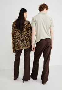 Leopard-patterned oversized sweater, brown striped trousers, light green polo, and high-heeled shoes. Neutral backdrop, focus on clothing details.