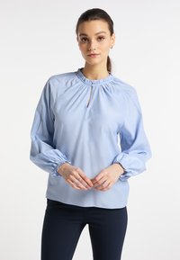 Jasnoniebieska bluzka z marszczonym dekoltem i detalem w kształcie dziurki, z długimi, bufiastymi rękawami z elastycznymi mankietami i gładką teksturą.