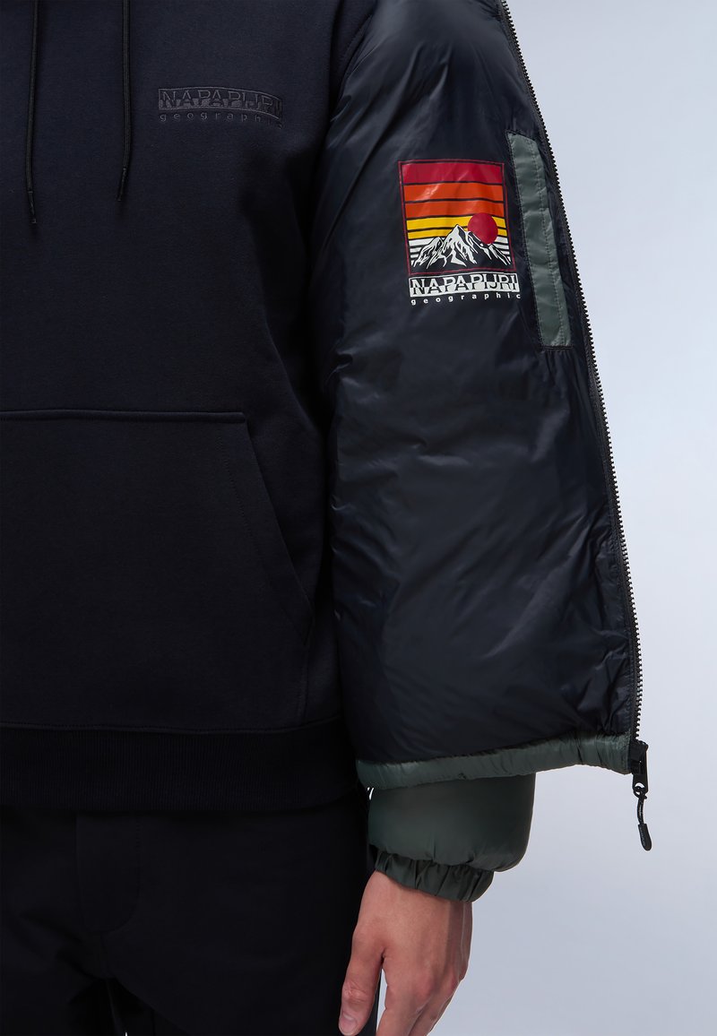 Schwarzer Hoodie mit einem puffigen schwarzen und grünen Ärmel. Verfügt über ein farbenfrohes Berglandschaft-Patch am Ärmel und eine frontale Kängurutasche.