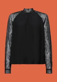 Blouse noire à manches longues avec manches en dentelle transparente et col montant en dentelle sur fond orange.