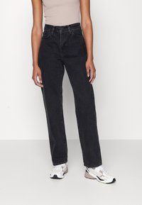 Høytlivte svarte denimjeans med rett ben. Har fem lommer og beltehemper. Kombinert med hvite og beige sneakers.
