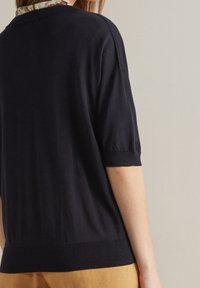 Černý pulover s krátkým rukávem a žebrovaným lemem a manžetami. Hladká textura, lehký materiál a volný střih.