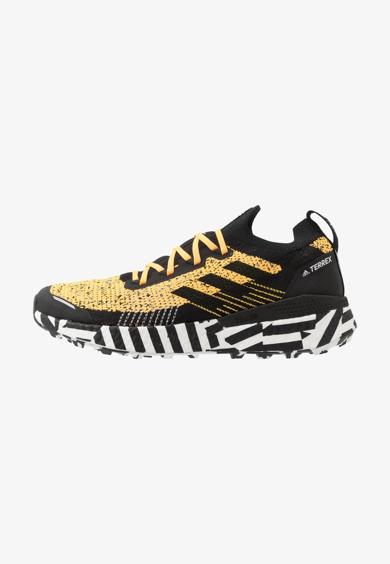 Chaussure de sport Adidas Terrex noire et jaune avec une semelle à motif noir et blanc et des lacets orange, vue du côté extérieur.