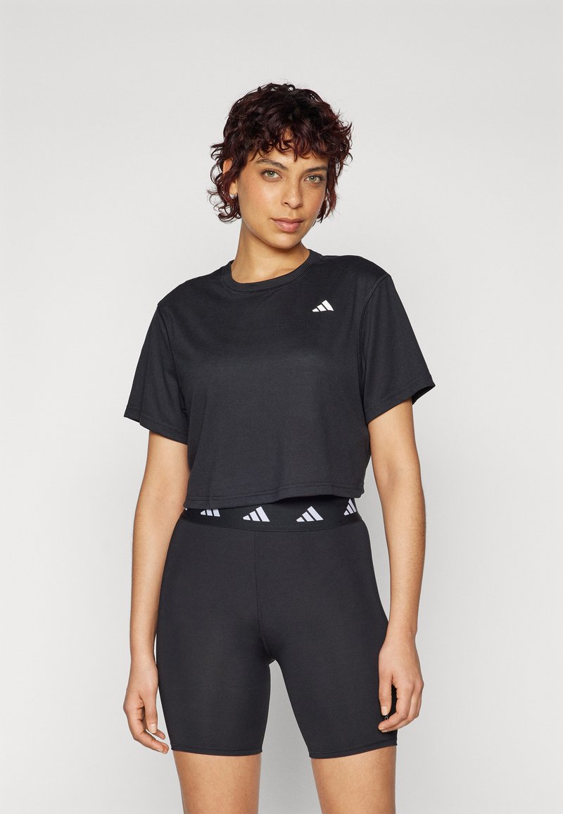 T-shirt noir court à manches courtes avec un petit logo blanc sur la poitrine, associé à un short noir ajusté avec une ceinture logo blanche.