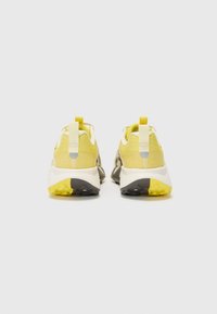 Baskets de sport avec une tige en mesh jaune, des accents gris et une semelle blanche texturée. Dotées d'une languette de traction et d'un motif de grip distinct sur la semelle.