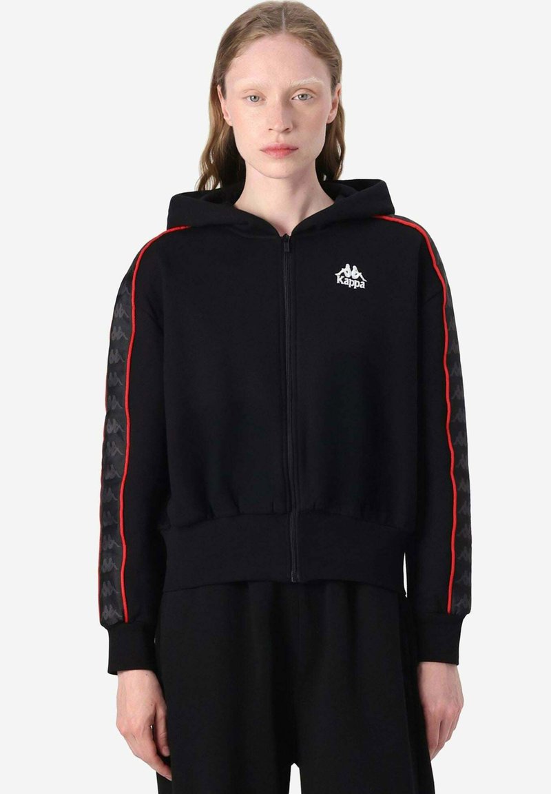 Felpa nera con zip, strisce laterali rosse, logo Kappa sul petto, maniche nere con motivo testurizzato, polsini e orlo a costine. Tessuto morbido.