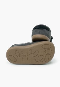 Scarpa per bambini di colore grigio scuro con suola marrone texturizzata, caratterizzata da modelli di presa a forma di piede e testo "Prodotto in Spagna".