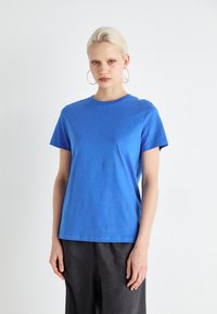Camiseta azul royal de manga corta hecha de algodón. Presenta un cuello redondo clásico y un corte relajado, combinada con pantalones gris de corte holgado.