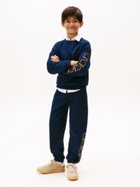 Felpa navy e pantaloni della tuta con motivi circolari ricamati. Sneakers beige e camicia colletto bianca sotto. Vestibilità comoda con polsini a coste.