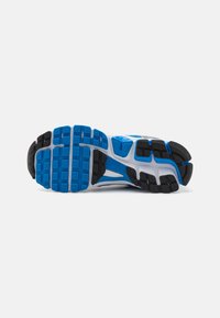 Semelle de chaussure de course en caoutchouc bleu et noir avec des motifs texturés pour l'adhérence ; accents blancs et gris sur les côtés.