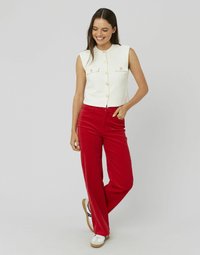 Haut court sans manches blanc avec fermeture à boutons et deux poches sur la poitrine, associé à un pantalon large en coton rouge et des baskets blanches.