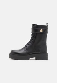 Bottes basses en cuir noir avec bout rond, design à lacets, semelle épaisse et une bride latérale avec un accent doré.