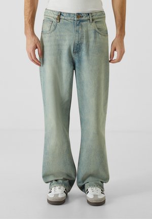 Light blue wide-leg jeans made of denim, featuring a faded wash, classic five-pocket design, and brown metal hardware. Paired with sneakers.