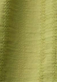 Gros plan sur un tissu vert clair tissé avec des rayures texturées verticales et des plis subtils.