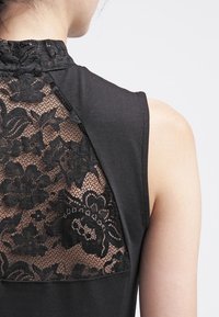 Haut du dos d'une femme portant un top noir sans manches avec un détail en dentelle florale sur le haut du dos et le cou.