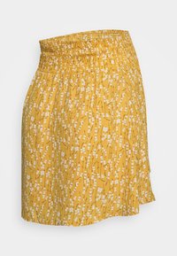 Jupe florale jaune avec une taille smockée, ornée de fleurs blanches et de délicates branches marron, fabriquée en tissu léger.