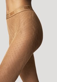 Nackte gemusterte Strumpfhosen mit strukturiertem Design und einem breiten, mit Markenzeichen versehenden elastischen Taillenbund. Das Material wirkt glatt und formbetont.