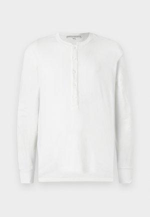 Camisa henley de manga larga blanca, hecha de algodón suave, con un escote redondo, una tapeta de botones y puños acanalados.