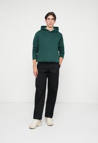 Roheline kapuutsiga sweatshirt, mis on valmistatud puuvillast, koos mustade pükste ja heledbež sneakeritega. Kitsas lõige, ribidega varrukate ja alläärega.