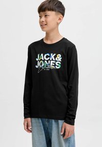 Rövid hajú fiú fekete, hosszú ujjú Jack & Jones ingben és világoskék farmernadrágban, mosolyogva néz oldalra.