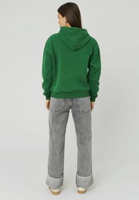 Sweat-shirt à capuche vert avec une coupe décontractée, associé à un jean large taille haute gris avec des ourlets effilochés et des poches arrière.