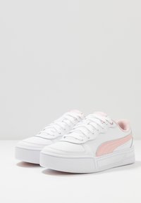 Białe sneakersy z różowymi akcentami, wykonane z gładkiego materiału syntetycznego, okrągły czubek, płaska podeszwa i sznurowanie. Zawierają logo po bokach.