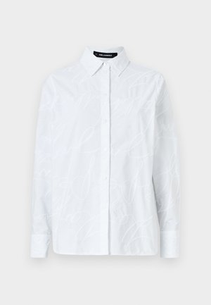 Camisa branca de botão, com um padrão de script texturizado, colarinho clássico, mangas longas e uma bainha reta. Feita de um tecido leve.