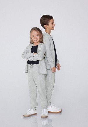 Hoodie et joggers en coton gris portés par deux enfants, avec un design zippé, une texture douce et des tailles élastiques avec cordons de serrage.