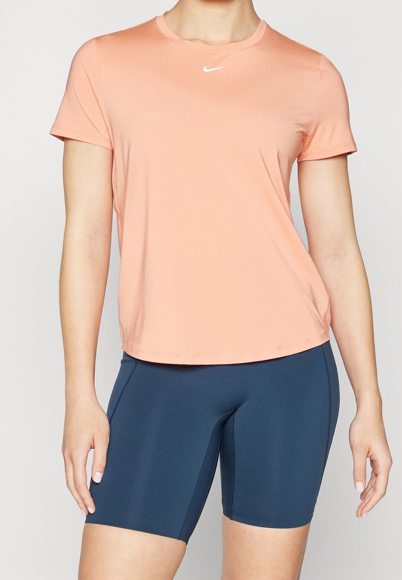 Camiseta deportiva de manga corta color rosa claro con cuello redondo y logo de Nike, combinada con pantalones cortos ajustados azul marino, con tela lisa y costuras.