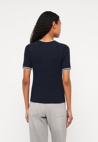 Ναυτικό μπλε πλεκτό μπλουζάκι κοντού μανικιού με υφή και άσπρες ρίγες στις μύτες και τα μανίκια. Εμφανίζεται η πίσω όψη.