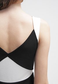 Czarna i biała sukienka z dekoltem w kształcie litery V na plecach, wyróżniająca się kontrastowymi kolorami, gładką fakturą i szerokimi ramiączkami, podkreślona geometrycznym wzorem.