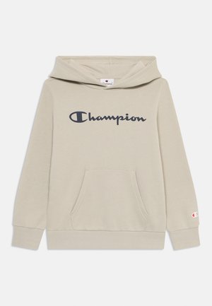 Haut à capuche beige clair en tissu doux, avec une poche frontale, un cordon de serrage au niveau de la capuche, et un logo "Champion" bleu foncé bien visible sur la poitrine.