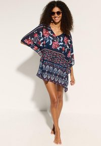 Kaftano floreale blu navy con maniche larghe, caratterizzato da motivi rossi e blu. Tessuto leggero e arioso; orlo asimmetrico con dettaglio a nodo.