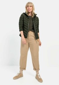 Grøn quiltet jakke med hætte, stribet top, beige afslappede bukser og brune sneakers. Simpelt design med tekstureret stof og synlige sømme.