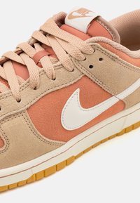 Nike-sneakers med en beige och korallfärgad mockaöverdel, vit Swoosh-logga och strukturerad gummisula i färgen gum.