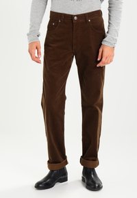 Bruna kordbyxor med slim fit, med knappslutning, två framfickor och uppvikta fållar, som bärs med svarta ankelstövlar.