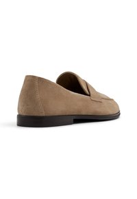 Un mocassin en daim marron clair avec une semelle noire basse, vu de dos sur fond blanc.