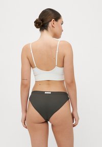 Witte geribbelde bralette met dunne bandjes en donkergroene high-waisted slips. Beide items hebben een gladde textuur en minimale details.