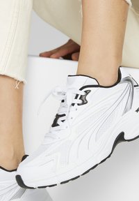 Baskets blanches de sport avec une tige en mesh et des accents noirs, bout rond, semelle contrastante et design à lacets.