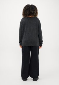 Mörkgrå oversize-tröja med vida ärmar, tillsammans med lösa svarta byxor. Mjuk textur, avslappnad passform och enkel design.